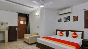 A bedroom with a bed, a desk, a chair, a ceiling fan, and an air conditioning unit. - Mauryan Elite I Hotel Hauzkhas  (New Delhi)