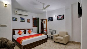 A hotel room with a bed, a chair, a ceiling fan, an air conditioner, and framed pictures on the walls. - Mauryan Elite I Hotel Hauzkhas  (New Delhi)