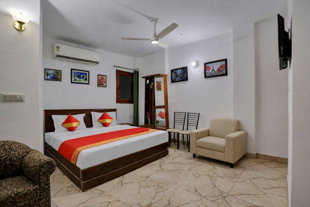 Una habitación de hotel con una cama, una silla, un ventilador de techo, aire acondicionado y cuadros en las paredes.