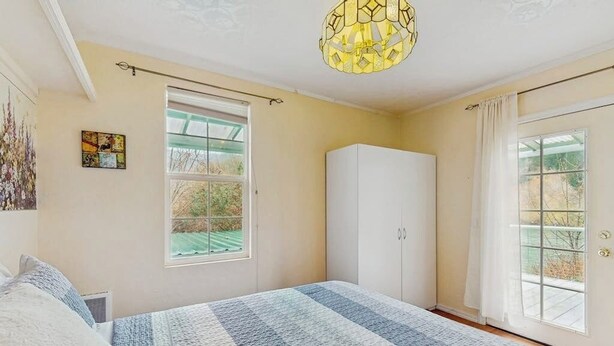 A bedroom with a large bed, a wardrobe, a window with a view, and a hanging light fixture. - Charming home on the Siuslaw River with a fire pit, WiFi,  & W&D (Mapleton)