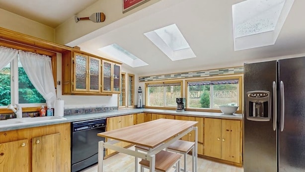 A kitchen with wooden cabinets, a stainless steel refrigerator, a dishwasher, and skylights.