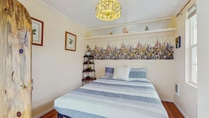 A bedroom with a bed, a chandelier, a floral wall decoration, and a wooden door.