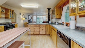 A kitchen with wooden cabinets, a central island, a dishwasher, and a window with curtains. - Charming home on the Siuslaw River with a fire pit, WiFi,  & W&D (Mapleton)