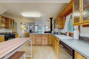 A kitchen with wooden cabinets, a central island, a dishwasher, and a window with curtains. - Charming home on the Siuslaw River with a fire pit, WiFi,  & W&D (Mapleton)