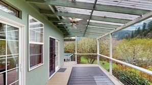 A covered porch with a ceiling fan, large windows, and a view of a garden. - Charming home on the Siuslaw River with a fire pit, WiFi,  & W&D (Mapleton)
