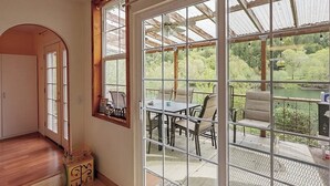 A room with a large window, a wooden door, and a view of an outdoor patio with a table and chairs. - Charming home on the Siuslaw River with a fire pit, WiFi,  & W&D (Mapleton)