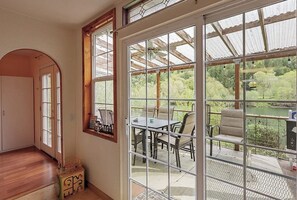 A room with a large window, a wooden door, and a view of an outdoor patio with a table and chairs. - Charming home on the Siuslaw River with a fire pit, WiFi,  & W&D (Mapleton)