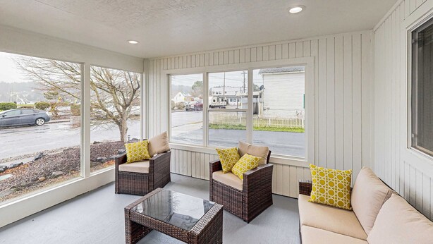 A covered porch with wicker furniture, a glass table, and a view of a street and houses. - Cozy condo with sun room, washer & dryer, close to the river (Florence)
