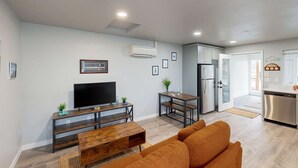 A modern living room with a flat-screen TV, wooden coffee table, and orange sofa. - Cozy condo with sun room, washer & dryer, close to the river (Florence)