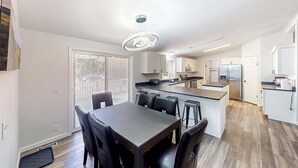 Une cuisine moderne dotée d’un îlot central, d’un coin repas avec une table et des chaises en bois foncé, et d’une grande fenêtre qui laisse entrer la lumière naturelle.
