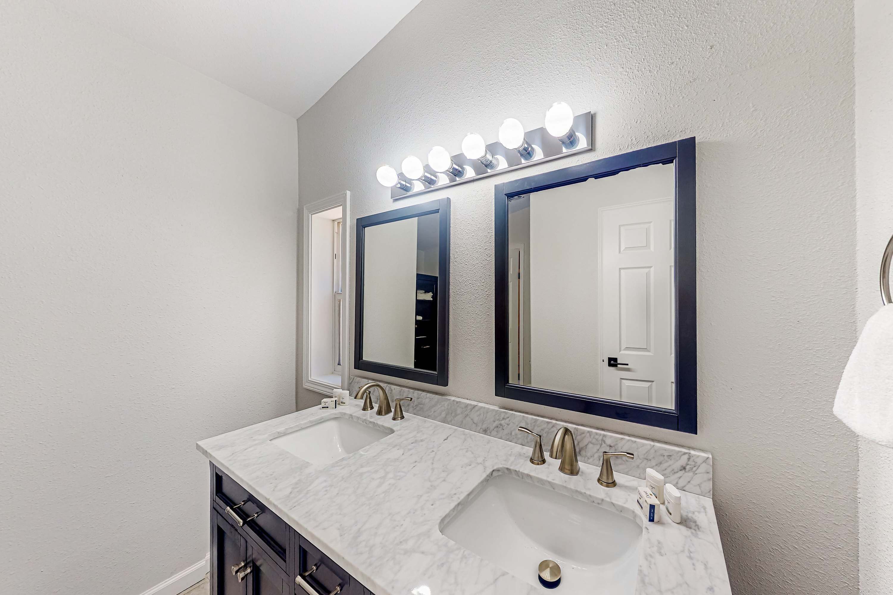 A bathroom with two sinks, a vanity, and three mirrors with lights.