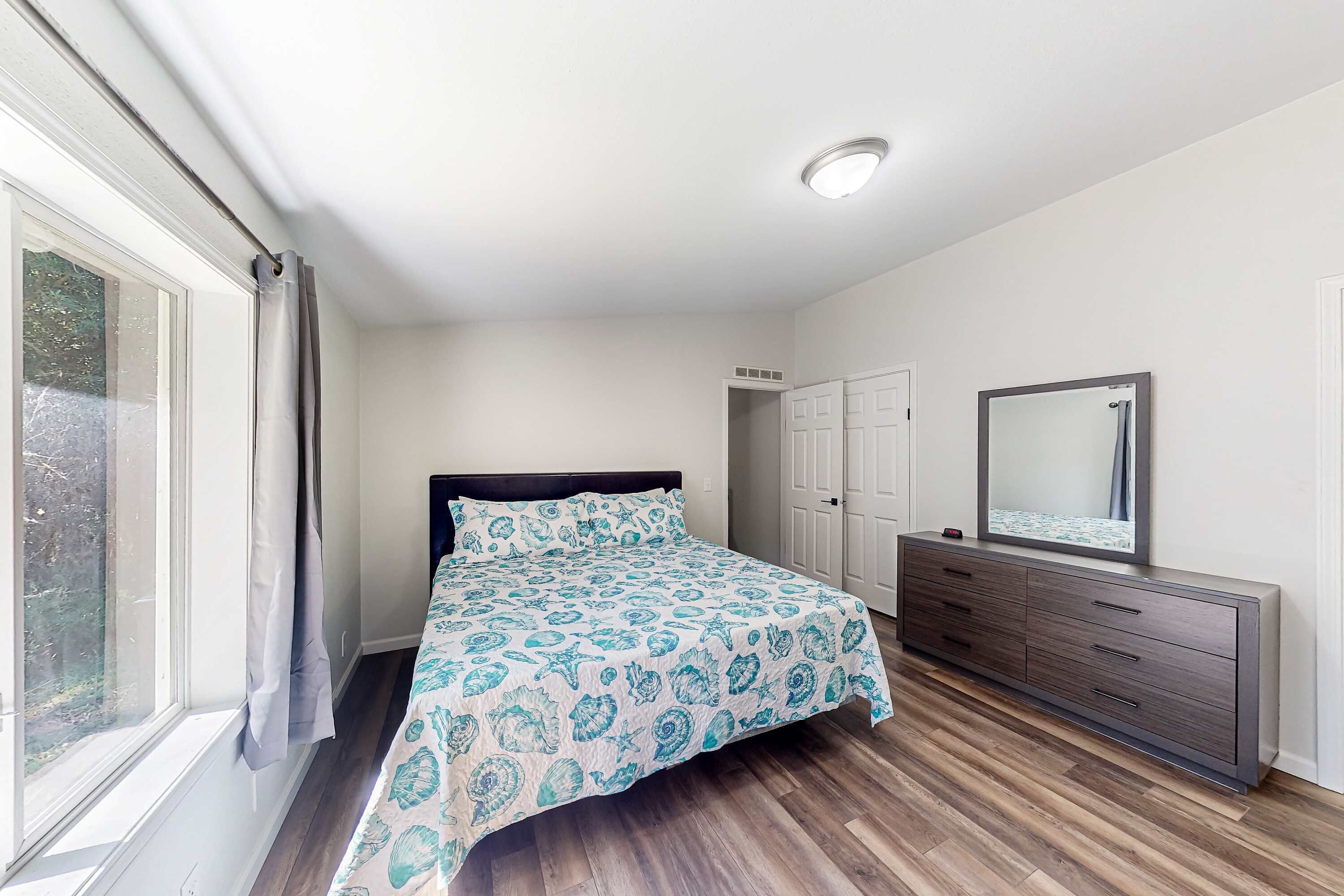 Un dormitorio con cama, cómoda, espejo y ventana.