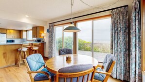 Een eetgedeelte met een ronde tafel, stoelen, een hanglamp en uitzicht door grote ramen.