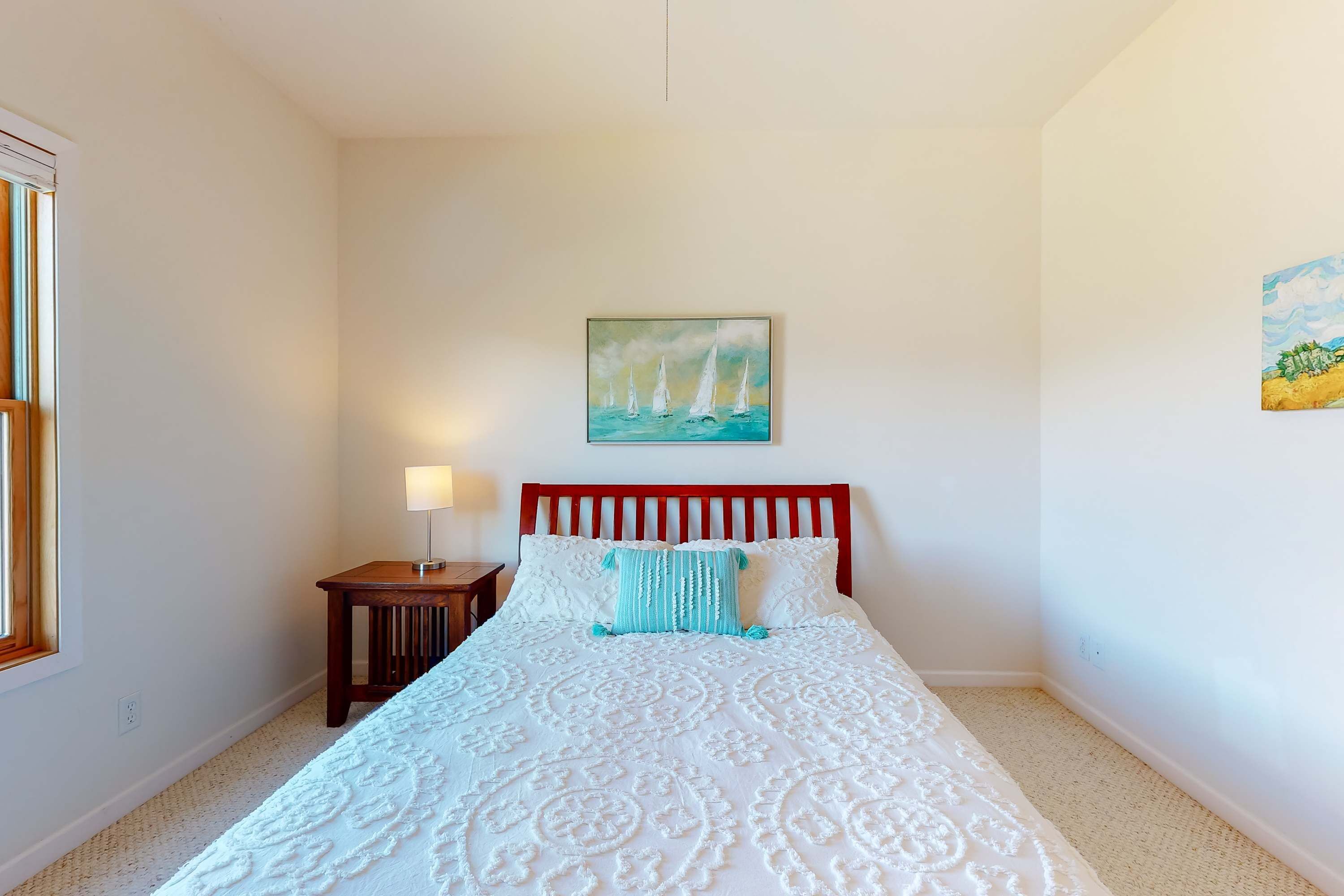A bedroom with a bed, a nightstand, a lamp, and two paintings on the wall.