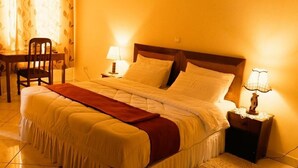 Una cama bien hecha con cabecera de madera, dos lámparas de noche y una silla en una habitación cálidamente iluminada.