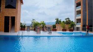 Una piscina con sillas de descanso, un edificio de fachada de ladrillo y vistas a colinas distantes.