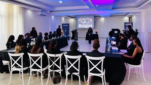Un salón de conferencias con un escenario, sillas blancas y una pantalla de proyecciones.