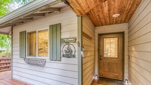 Fachada de madera con un letrero de bienvenida, una puerta con un panel de vidrio y un ventanal con contraventanas.