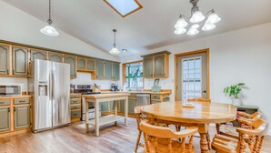 Una cocina moderna con armarios de madera, un refrigerador de acero inoxidable, una mesa de comedor de madera y lámparas colgantes.