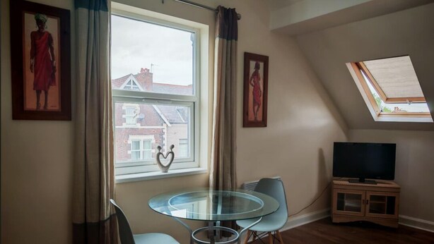 A room with a round glass table, two chairs, a television, and framed artwork on the walls. - 1 Bedroom apartment - Clarendon 69 (Wallasey)