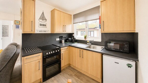 A compact kitchen with wooden cabinets, a black stove, a microwave, and a small refrigerator.