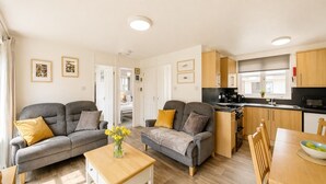 A modern living room with two sofas, a coffee table, and a kitchen area with wooden cabinets and appliances. - 57 Trevithick Court, Tolroy Manor (Tolroy Manor)