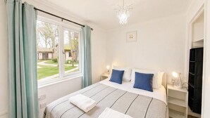 A bedroom with a bed, curtains, a chandelier, bedside lamps, and a window with a view. - 57 Trevithick Court, Tolroy Manor (Tolroy Manor)