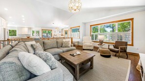 A spacious living room with a large sectional sofa, a wooden coffee table, and a view of the kitchen through large windows. - Spacious home with fenced yard, deck, grill, fast WiFi, & game room (Cannon Beach)