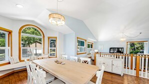 A spacious kitchen with a large wooden table, white chairs, and a built-in island with a white railing. - Spacious home with fenced yard, deck, grill, fast WiFi, & game room (Cannon Beach)