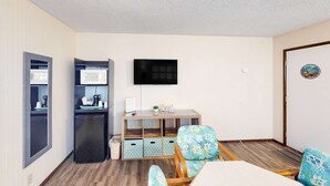 A compact living space with a kitchenette, a flat-screen TV, a dining table, and a patterned chair. - Retro-chic room near beach with fast WiFI - walk to downtown shops & eateries (Bandon)