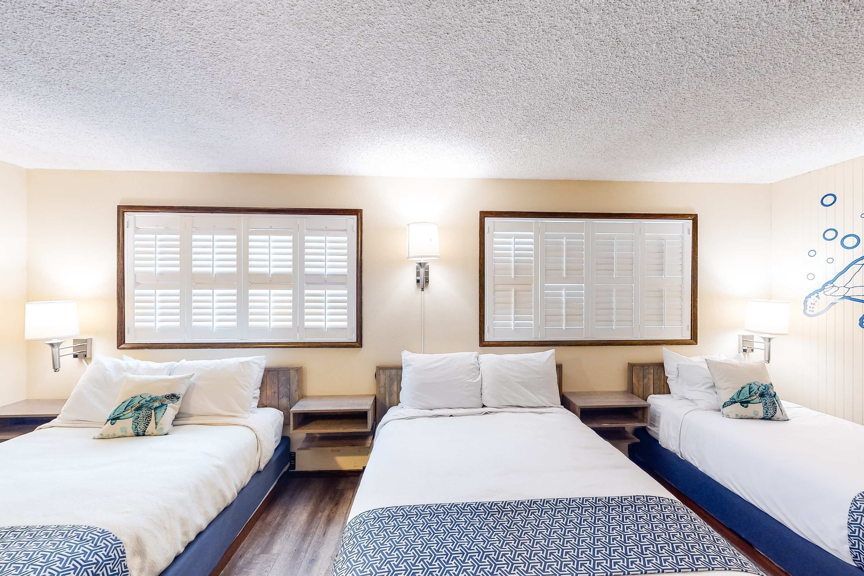 Habitación de hotel con dos camas, una ventana con contraventanas, una lámpara de pared y un adorno mural.