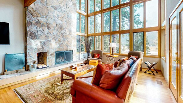 A spacious living room with a stone fireplace, large windows, a leather sofa, and a wooden coffee table.