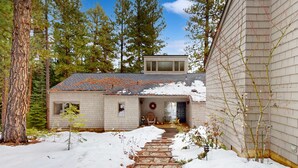A house with a stone pathway leading to the entrance, surrounded by snow and trees.