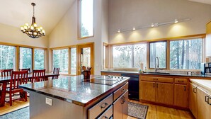 A spacious kitchen with a large island, wooden cabinets, and large windows offering a view of trees.