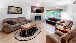A living room with a fireplace, a television, a ceiling fan, and a large window. - Large Dog-Friendly Duplex with Lovely Interior + Free WiFi, Private Washer/Dryer (Joseph)