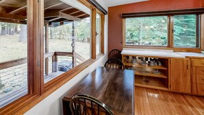 A wooden dining table with chairs, a window with a view of trees, and a shelf with dishes. - Large Dog-Friendly Duplex with Lovely Interior + Free WiFi, Private Washer/Dryer (Joseph)