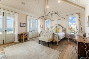 A bedroom with a four-poster bed, a chair, a small table, and a view of the sea through large windows. - Seagrove "Belle Plage" 517 Eastern Lake Rd (Santa Rosa Beach)