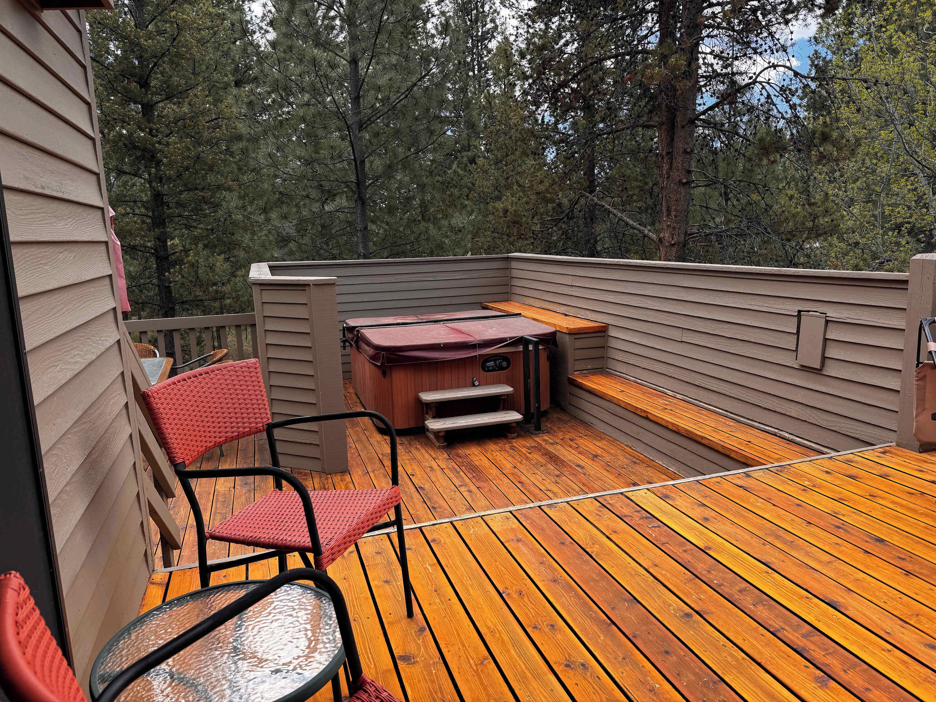 A deck with a hot tub, a table, and chairs.