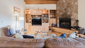 Ein gemütliches Wohnzimmer mit Kamin aus Stein, Holzmöbeln und einem Flachbildfernseher.