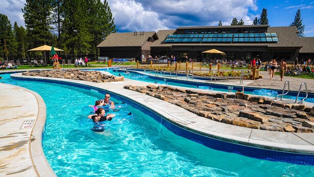 Ein Schwimmbecken mit mehreren Bahnen, Liegestühlen und einem Gebäude mit großen Fenstern im Hintergrund.