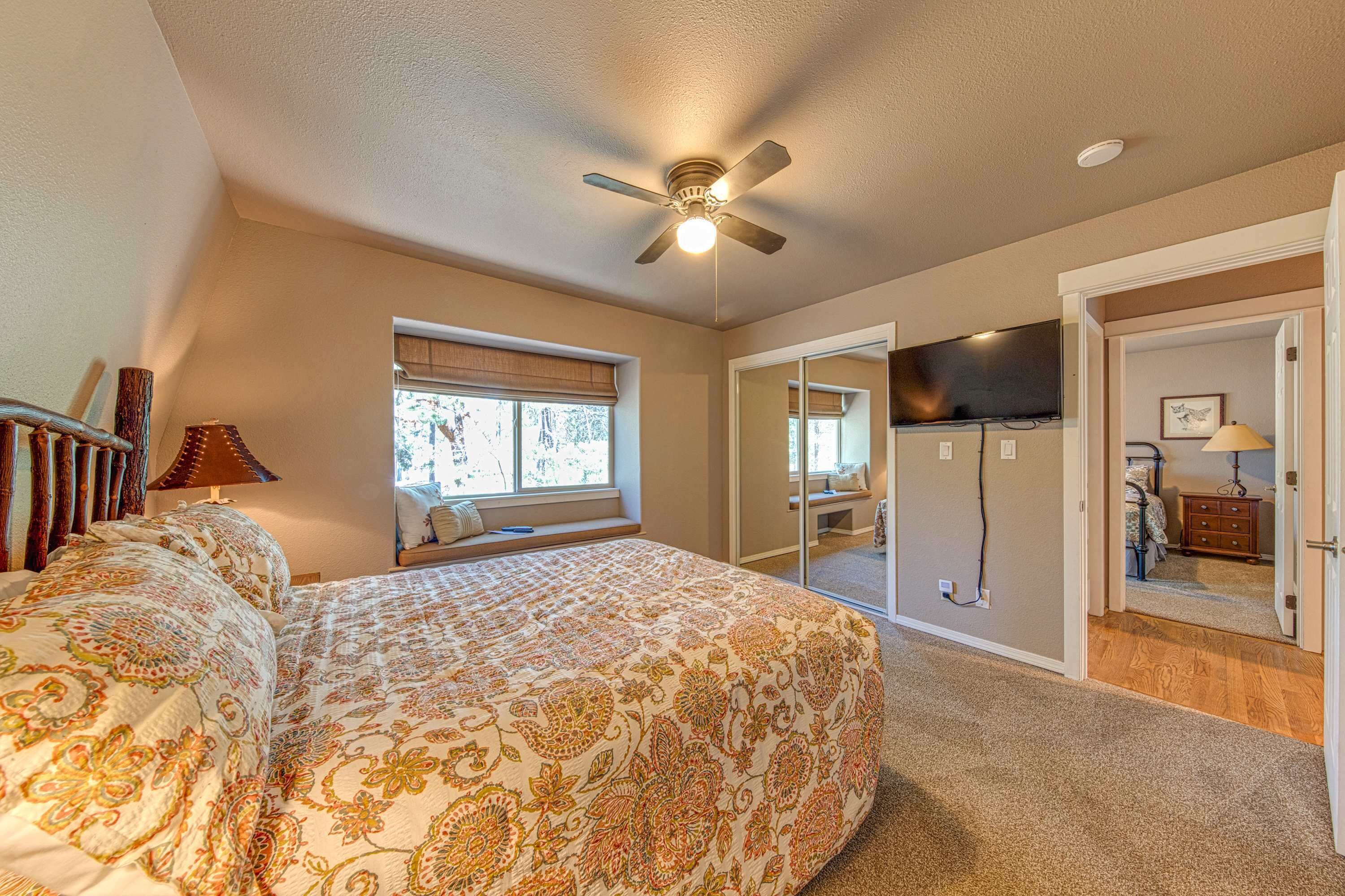 A bedroom with a large bed, a ceiling fan, a TV, and a window with blinds.