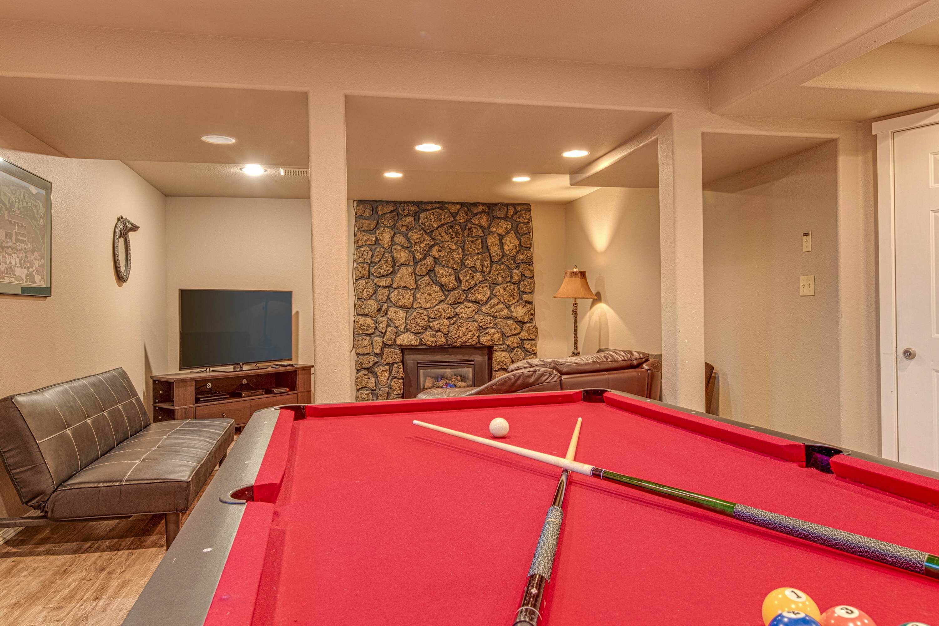 A pool table with balls and cues, a sofa, a television, and a stone wall.