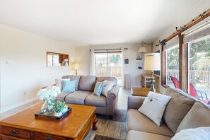 A living room with a sofa, a coffee table, and a lamp. There is a window with curtains and a view of the outside. - Dog-friendly house on Alsea Bay with bridge views, grill & private hot tub (Waldport)