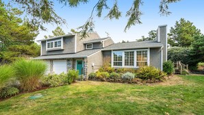 Une maison à deux étages avec un garage, entourée d’une pelouse bien entretenue et de divers arbustes.