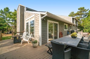 Une maison avec une terrasse, un barbecue, du mobilier d’extérieur et une grande fenêtre.