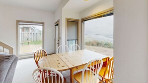 Un comedor con mesa y sillas de madera, ventanas amplias y vista a una terraza de madera.