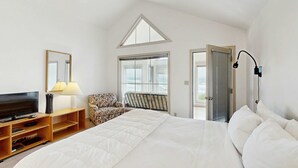 Un dormitorio con cama, televisión, lámpara, silla y puerta al balcón.
