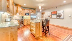 Una cucina con mobili in legno, piani in granito, forno a microonde integrato e un bancone con sgabelli.