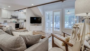 Ein modernes Wohnzimmer mit einer Couch, Fernseher und Blick auf eine verschneite Landschaft.