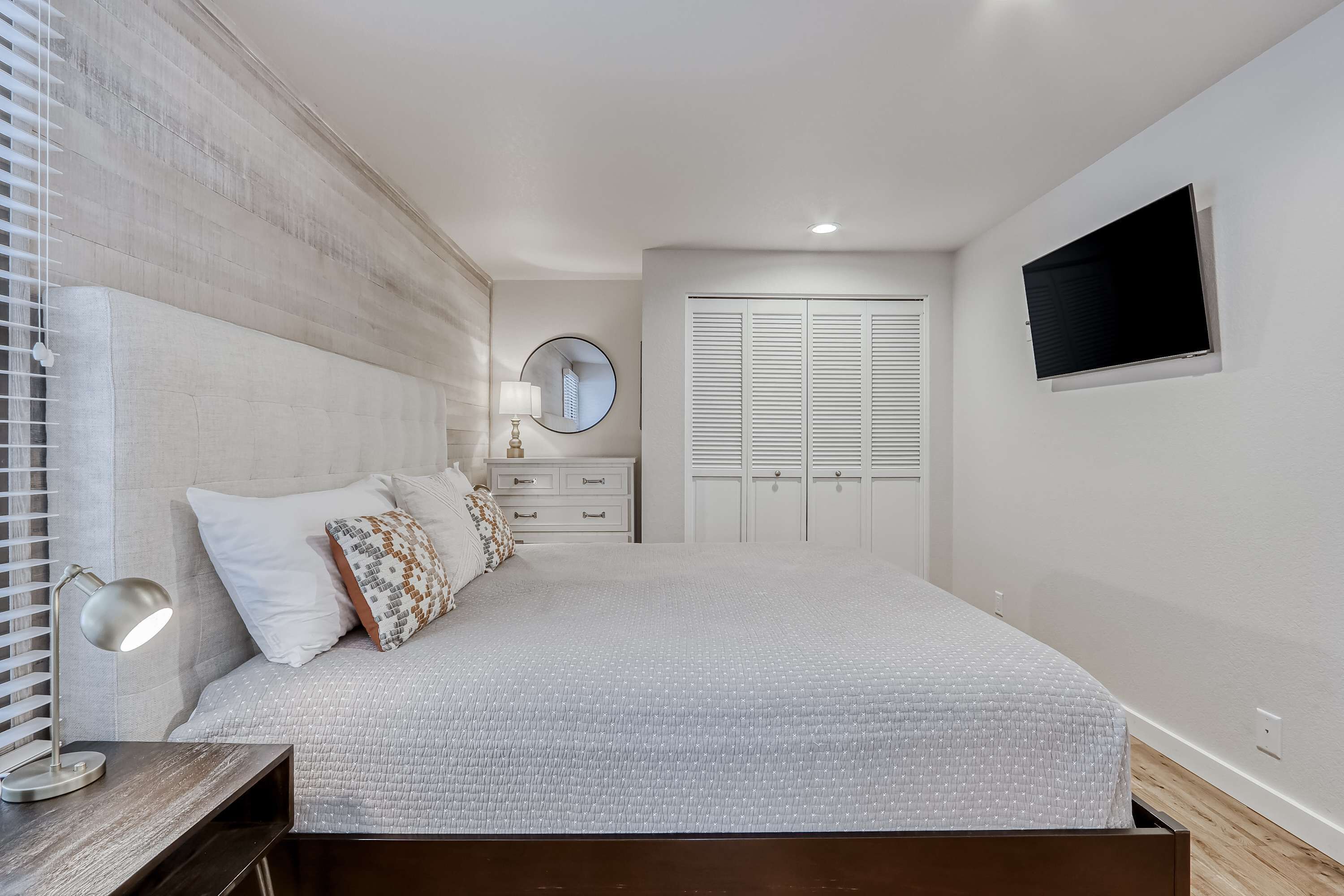 Une chambre à coucher comprenant un lit, une table de chevet, une lampe, une commode, un miroir, un placard et un téléviseur.